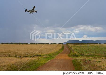 Landscape with a road in the savannah and an airplane in the sky Landscape with a road in the savannah and an airplane in the sky 105360867