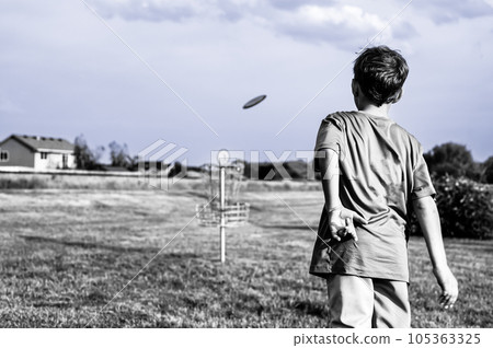 Young Caucasian male boy aiming a disc golf at a chain goal. Young Caucasian male boy aiming a disc golf at a chain goal. 105363325