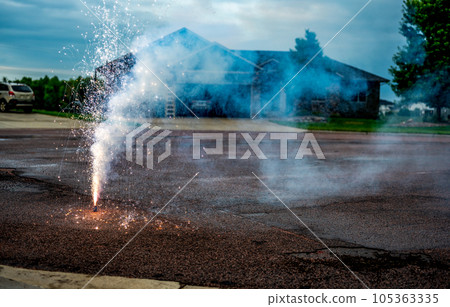 A fountain of sparks, flames, and smoke emitting from a fountain fireworks being set off in a residential neighborhood. A fountain of sparks, flames, and smoke emitting from a fountain fireworks being set off in a residential neighborhood. 105363335