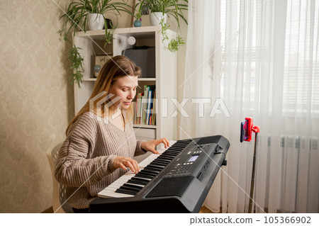 Woman learns music, playing piano online at home interior. 105366902