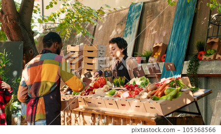 Diverse team of farmers helping clients choose organic produce, selling homegrown bio fruits and vegetables. Local vendor showing eco fresh natural products at street greenmarket. Diverse team of farmers helping clients choose organic produce, selling homegrown bio fruits and vegetables. Local vendor showing eco fresh natural products at street greenmarket. 105368566
