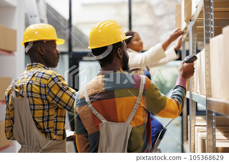 Shipment department workers using barcode scanner in warehouse. African american logistics managers scanning cardboard boxes and analyzing freight storing in industrial storehouse 105368629