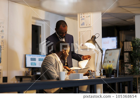 African american men analyzing financial statistics typing company strategy on computer, discussing investment growth report. Executive managers working late at night in startup office African american men analyzing financial statistics typing company strategy on computer, discussing investment growth report. Executive managers working late at night in startup office 105368654