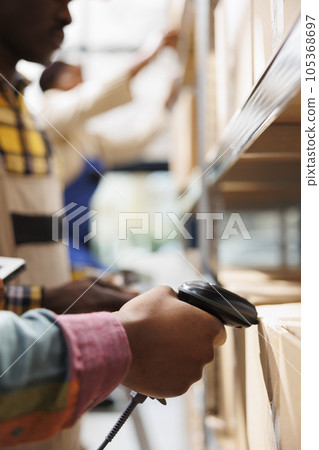 African american postal worker hand scanning parcel barcode in warehouse. Post office storehouse employee arm using qr code scanner tool on customer package before delivery close up African american postal worker hand scanning parcel barcode in warehouse. Post office storehouse employee arm using qr code scanner tool on customer package before delivery close up 105368697
