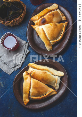 Tipical Chilean baked empanadas de pino y napolitano on clay plates with wine. Dish and drink on 18 September party Independence day Chile, blue background. 105369641