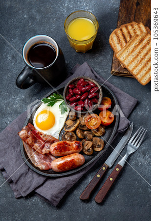 Full fry up English breakfast with fried eggs, sausages, bacon, black pudding, beans, toast and coffee, dark background 105369643