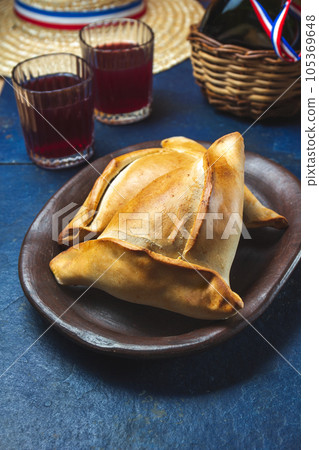 Tipical Chilean baked empanadas de pino y napolitano on clay plates with wine. Dish and drink on 18 September party Independence day Chile, blue background. 105369648