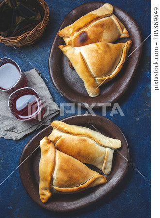 Tipical Chilean baked empanadas de pino y napolitano on clay plates with wine. Dish and drink on 18 September party Independence day Chile, blue background. 105369649
