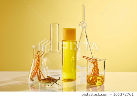 A bottle unlabeled filled with yellow liquid decorated with cordyceps and laboratory equipment on yellow background. Advertising photo, space for design 105372761