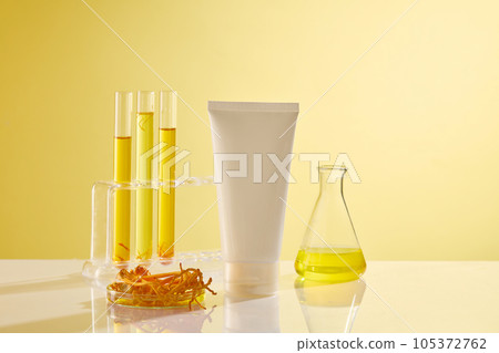 Front view of a white plastic tube unbranded decorated with cordyceps, test tube and erlenmeyer flasks filled with yellow liquid on yellow background. Mockup for advertising, space for design 105372762