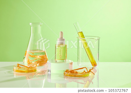 Against the green background, glass flask containing cordyceps and yellow liquid decorated with a serum bottle unbranded. Mockup scene for advertising cosmetic of cordyceps extract Against the green background, glass flask containing cordyceps and yellow liquid decorated with a serum bottle unbranded. Mockup scene for advertising cosmetic of cordyceps extract 105372767