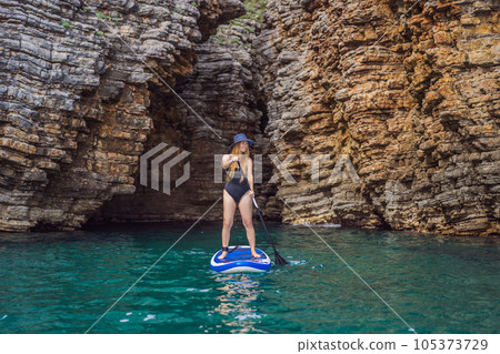 Young women Having Fun Stand Up Paddling in blue water seaamong the rocks in Montenegro. SUP 105373729