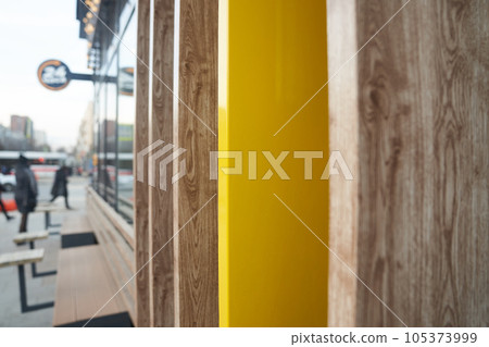 A fragment of a wall at the intersection of several natural-colored boards, a view of the street along the wall. Unrecognizable people near the cafe. High quality photo 105373999