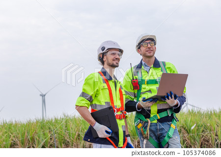 Teamwork engineer worker wearing safety uniform using laptop at wind turbine field renewable energy. Teamwork engineer worker wearing safety uniform using laptop at wind turbine field renewable energy. 105374086