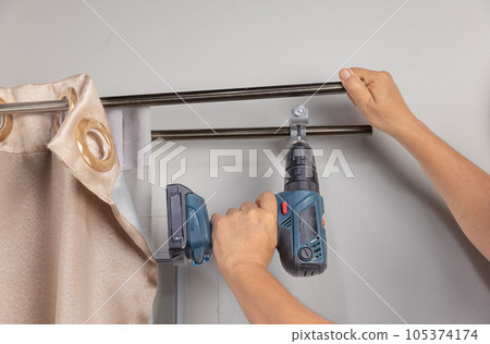 Worker repairman hanging and fixing the curtain on the window Worker repairman hanging and fixing the curtain on the window 105374174