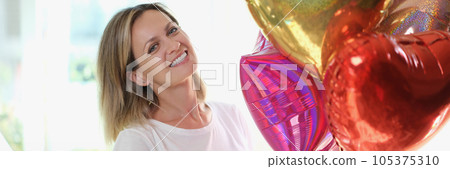 Pleased blonde woman smiling and holding many air baloons in hand. 105375310