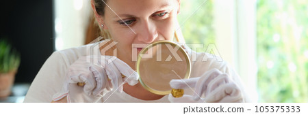 Female expert checks gold coin with magnifying glass. 105375333