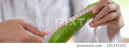 Doctor hands holding long vegetable and measuring tape above table in medical clinic. Doctor hands holding long vegetable and measuring tape above table in medical clinic. 105375345