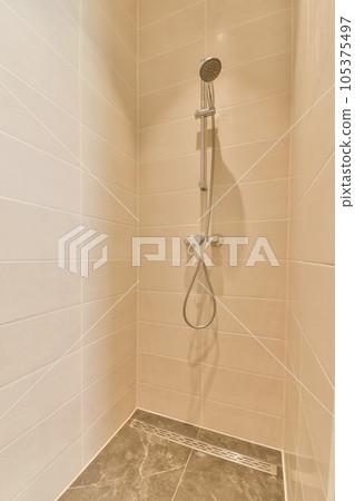 a shower room with tile flooring and beige tiles on the walls, there is a hand held shower head 105375497