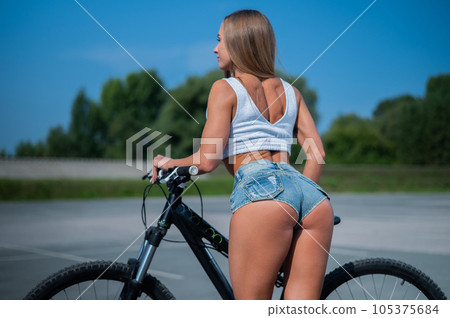 Caucasian woman in short shorts rides a bike on a hot summer day. Caucasian woman in short shorts rides a bike on a hot summer day. 105375684