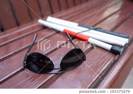 Sunglasses and a folding cane for the blind on a bench. Sunglasses and a folding cane for the blind on a bench. 105375879