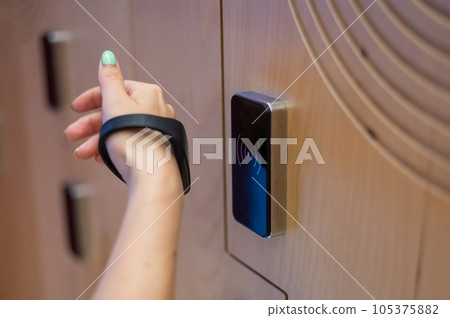 A woman opens the electronic lock of a cubicle in a locker room with a bracelet. A woman opens the electronic lock of a cubicle in a locker room with a bracelet. 105375882