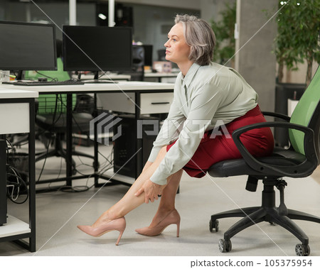 Caucasian woman massaging her tired legs while sitting in the office. Caucasian woman massaging her tired legs while sitting in the office. 105375954
