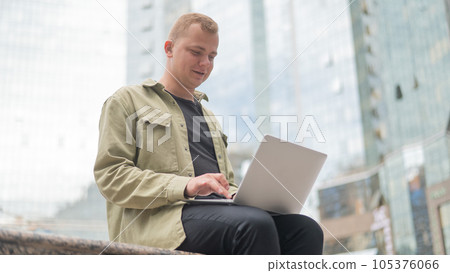 Thoughtful joyful guy with hearing aid using laptop outdoors.  105376066