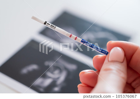 Woman holding a positive pregnancy test on the background of a photo with an ultrasound.  105376067