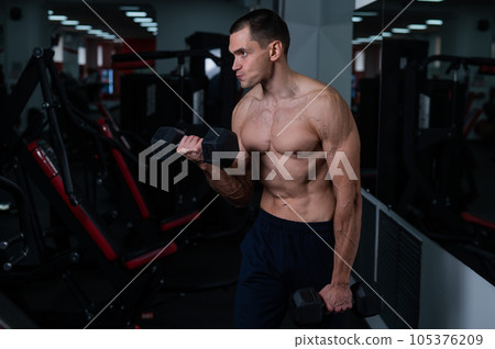 Shirtless man doing bicep exercises with dumbbells in the gym. Shirtless man doing bicep exercises with dumbbells in the gym. 105376209