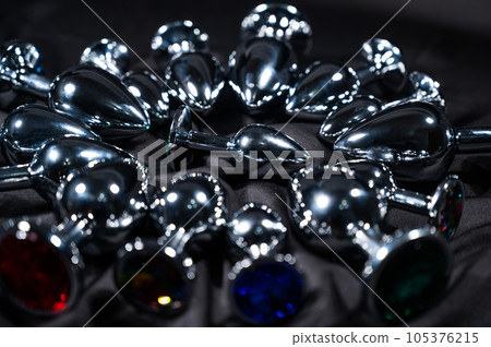 Many metal anal plugs on a black silk sheet.  105376215
