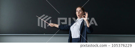 Red-haired caucasian woman in a pantsuit shows an ok sign. Surprised female teacher with a pointer at the blackboard. Widescreen. Red-haired caucasian woman in a pantsuit shows an ok sign. Surprised female teacher with a pointer at the blackboard. Widescreen. 105376229