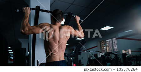 Back view of shirtless man with pull-ups in gym.  105376264