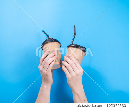 A woman holds two cardboard cups with coffee on a blue background. 105376280