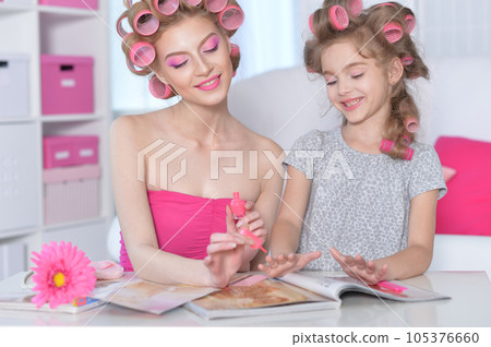 Mom and daughter with hair curlers reading magazine Mom and daughter with hair curlers reading magazine 105376660