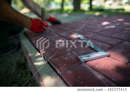 The protractor lies on the paving stones and the worker lays the pavement. 105377415