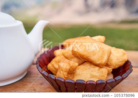 Teapot with tea and delicious National Kazakh pastries baursak. Street cafe in the highlands with a view of the mountains.. Fry dough in boiling oil in a frying pan. Teapot with tea and delicious National Kazakh pastries baursak. Street cafe in the highlands with a view of the mountains.. Fry dough in boiling oil in a frying pan. 105378096