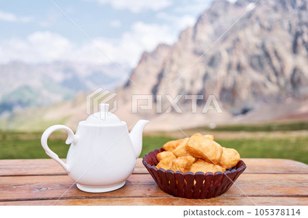Teapot with tea and delicious National Kazakh pastries baursak. Street cafe in the highlands with a view of the mountains.. Fry dough in boiling oil in a frying pan. Teapot with tea and delicious National Kazakh pastries baursak. Street cafe in the highlands with a view of the mountains.. Fry dough in boiling oil in a frying pan. 105378114