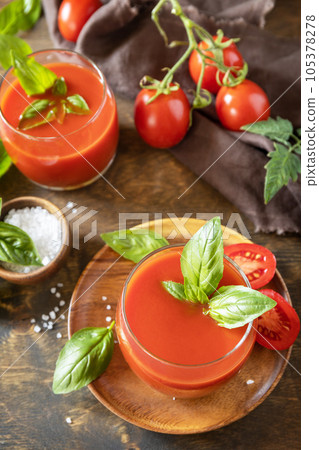 Glasses of fresh tomato juice with tomatoes, salt on wooden table. Vegetable tomato drink for a healthy diet. Glasses of fresh tomato juice with tomatoes, salt on wooden table. Vegetable tomato drink for a healthy diet. 105378278