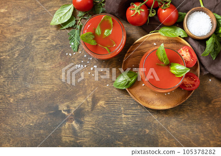 Glasses of fresh tomato juice with tomatoes, salt on wooden table. Vegetable tomato drink for a healthy diet. View from above. Copy space. Glasses of fresh tomato juice with tomatoes, salt on wooden table. Vegetable tomato drink for a healthy diet. View from above. Copy space. 105378282
