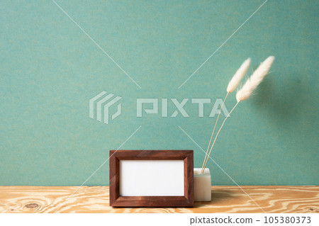 Minimal wooden picture frame with dry flower on wooden table. green wall background. copy space 105380373
