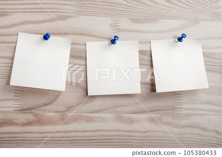 Three white paper notes mockup pinned to wooden bulletin board. sticky notes on bulletin board. Three sticker with push pins on wooden background Three white paper notes mockup pinned to wooden bulletin board. sticky notes on bulletin board. Three sticker with push pins on wooden background 105380433