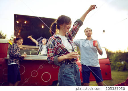 Young people attending outdoor party in countryside dancing, drinking cocktails, having fun together on warm summer evening 105383050