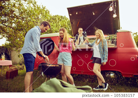 Friends meeting in countryside on warm summer day, having picnic and barbecue, cooking meat and cocktails, talking and having good time 105383157