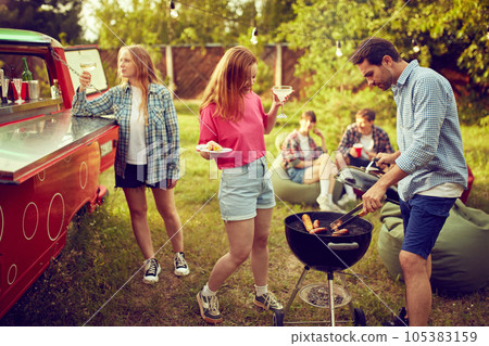 Group of young people, friends spending time outdoors, having barbecue party, cooking, drinking cocktails, talking. Countryside meeting Group of young people, friends spending time outdoors, having barbecue party, cooking, drinking cocktails, talking. Countryside meeting 105383159