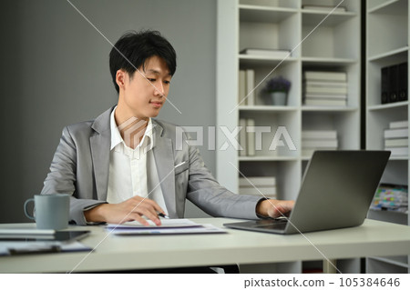 Millennial businessman wearing formal wear working with statistical document in modern office 105384646