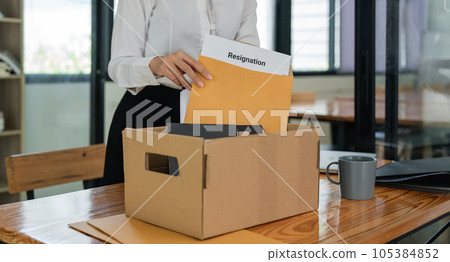 Asian female office worker carrying a cardboard box with her personal stuff and resignation letter 105384852