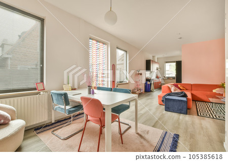 a living room with pink and blue chairs, an orange couch, and a white table in front of the window a living room with pink and blue chairs, an orange couch, and a white table in front of the window 105385618