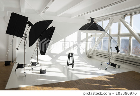 Professional lighting equipment, ligts, stands, soft boxeson a white huge big cyclorama in modern photo studio with a big daylight windows. 105386970
