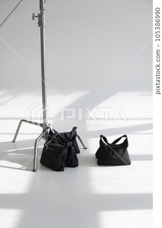 Three sand bags on a studio cyclorama with a stand, c-stand. Photography studio sandbags for photographic equipment. Ballast for lighting stands. Three sand bags on a studio cyclorama with a stand, c-stand. Photography studio sandbags for photographic equipment. Ballast for lighting stands. 105386990